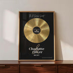 Personalised couple print with a gold vinyl record on a black background, featuring five sense-themed love messages and line-art faces, the names Charlotte & Oliver and the date 09.07.2011 below, in a timber frame resting on a wooden sideboard.