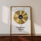 Personalised couple print with a gold vinyl record on a cream background, featuring five sense-themed love messages and line-art faces, the names Charlotte & Oliver and the date 09.07.2011 below, in a timber frame resting on a wooden sideboard.