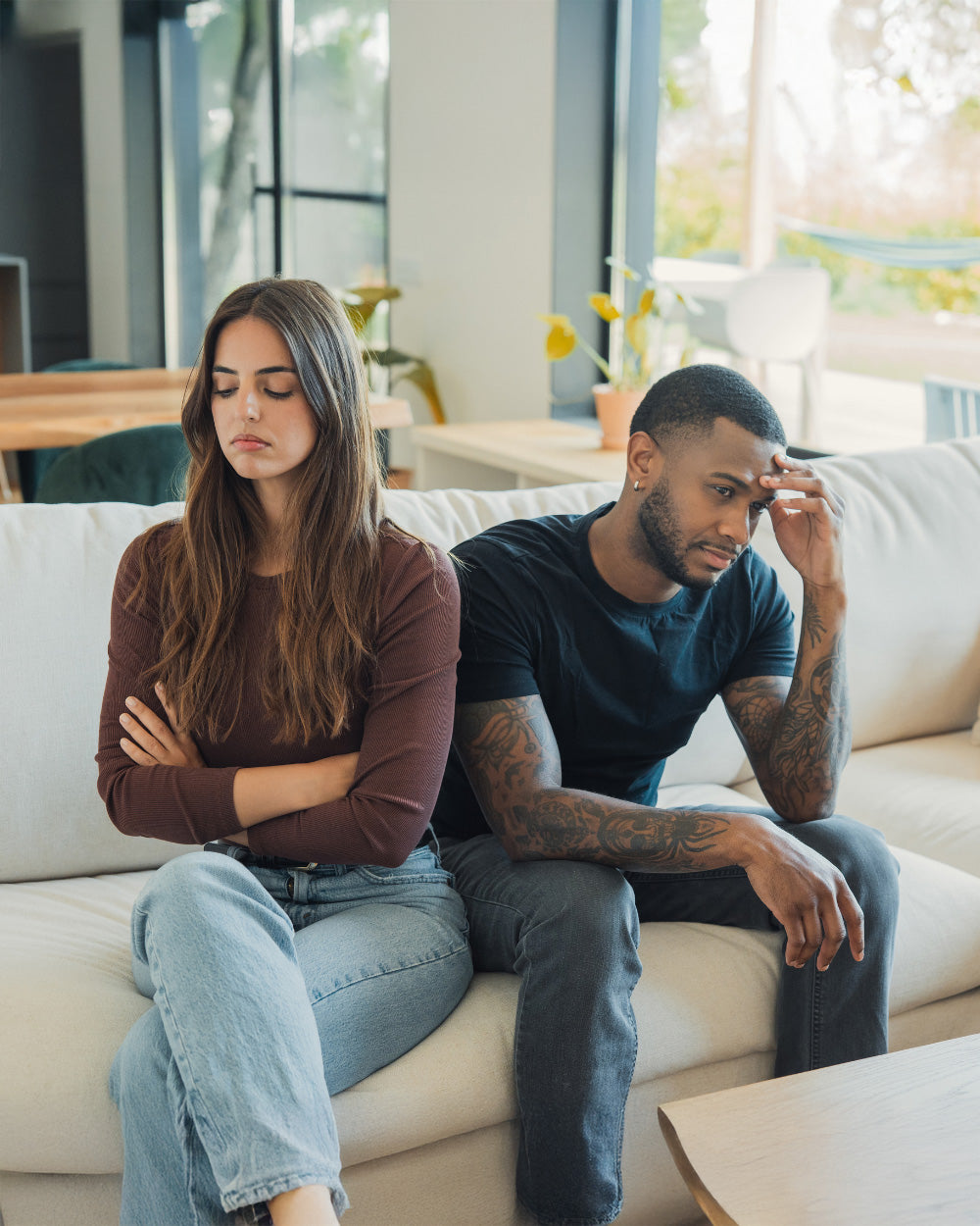 A couple sitting apart on a sofa, both looking away, showing the quiet distance that can grow in a marriage