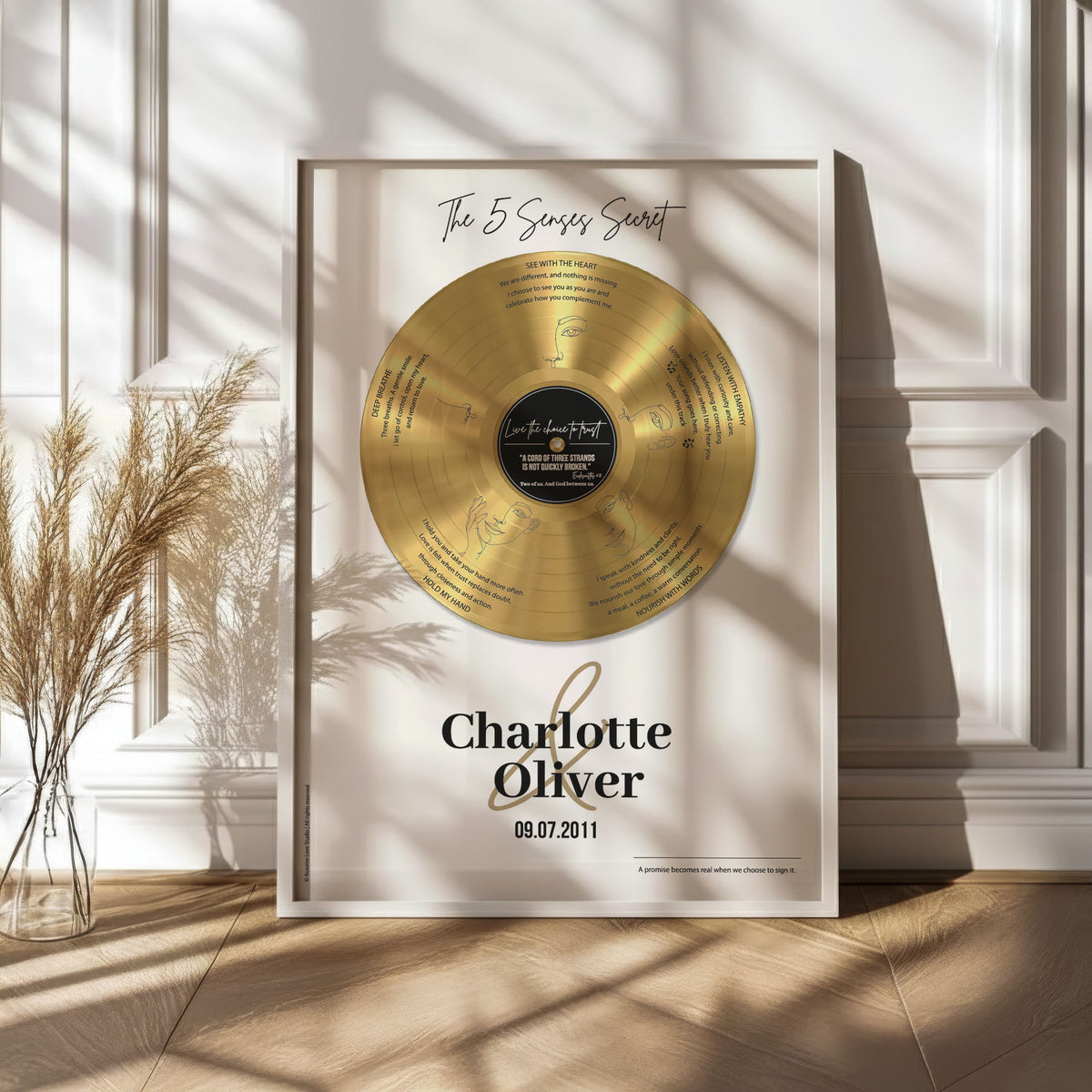 Personalised couple print with a gold vinyl record on a cream background, featuring five sense-themed love messages and line-art faces, the names Charlotte & Oliver and the date 09.07.2011 below, in a white frame.